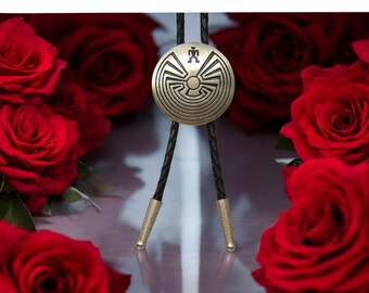 Könnte beinhalten: Ein goldener Bolo-Schlips mit einem runden Anhänger mit einem indianischen Design. Der Anhänger hat ein Labyrinthmuster und eine kleine Figur in der Mitte. Der Bolo-Schlips ist von roten Rosen umgeben.