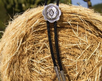 Könnte beinhalten: Ein silberner Bolo-Schal mit einem diamantförmigen Design in der Mitte des Bolos. Der Bolo liegt auf einem Heuballen.