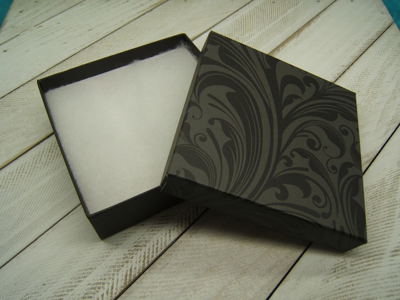 Puede incluir: Una caja de regalo negra con un interior blanco y un patr&oacute;n floral negro y gris en la tapa.