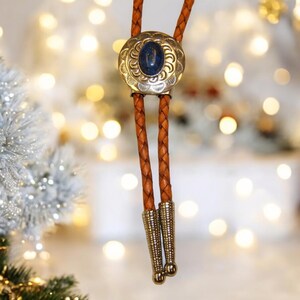 May include: A brown leather bolo tie with a silver and blue stone centerpiece. The tie has a braided design and silver tips.