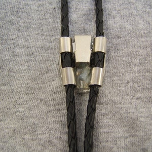 May include: A black bolo tie with a silver clasp. The bolo tie is made of braided leather and has a silver tip.