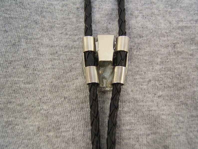 May include: A black bolo tie with a silver clasp. The bolo tie is made of braided leather and has a silver tip.