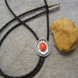 Puede incluir: Un corbatín de cuero negro con un deslizador de corbatín de plata y piedra roja.