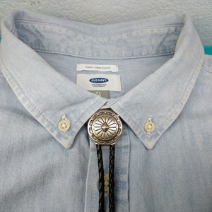 May include: A light blue denim shirt with a silver bolo tie featuring a floral design. The shirt has a button-down collar and a label that reads "Old Navy" and "XL".