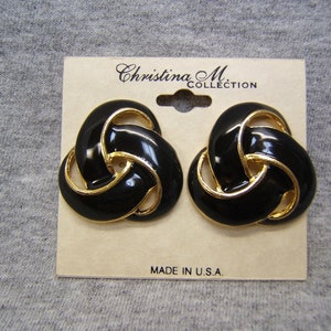 May include: A pair of gold-tone earrings with black enamel. The earrings are shaped like a knot and have a gold trim. The earrings are on a card that says "Christina M. Collection" and "Made in U.S.A."