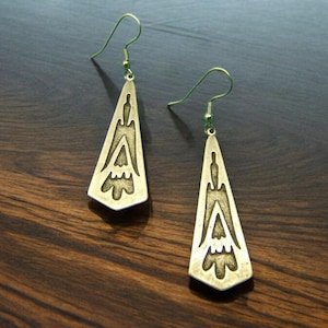 May include: A pair of gold-toned earrings with a geometric design. The earrings are shaped like triangles with intricate patterns.