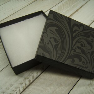 May include: A black gift box with a white foam interior and a black and gray floral pattern on the lid.