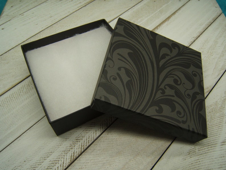 May include: A black gift box with a white foam interior and a black and gray floral pattern on the lid.