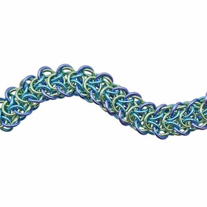 Puede incluir: Un brazalete de malla de cadena azul y verde con un cierre de palanca plateado y un colgante de plata martillado.