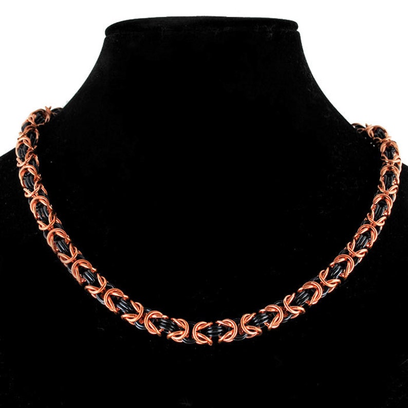 May include: A black and copper chainmail necklace. The chainmail is made of small, interlocking metal rings.