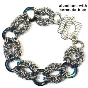 May include: Three chainmail bracelets with different metal finishes and iridescent accents. The top bracelet is gold with a blue and green iridescent accent. The middle bracelet is silver with a blue iridescent accent. The bottom bracelet is copper with a blue and purple iridescent accent.
