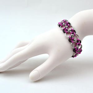 May include: A black and pink chainmail bracelet with silver rings.