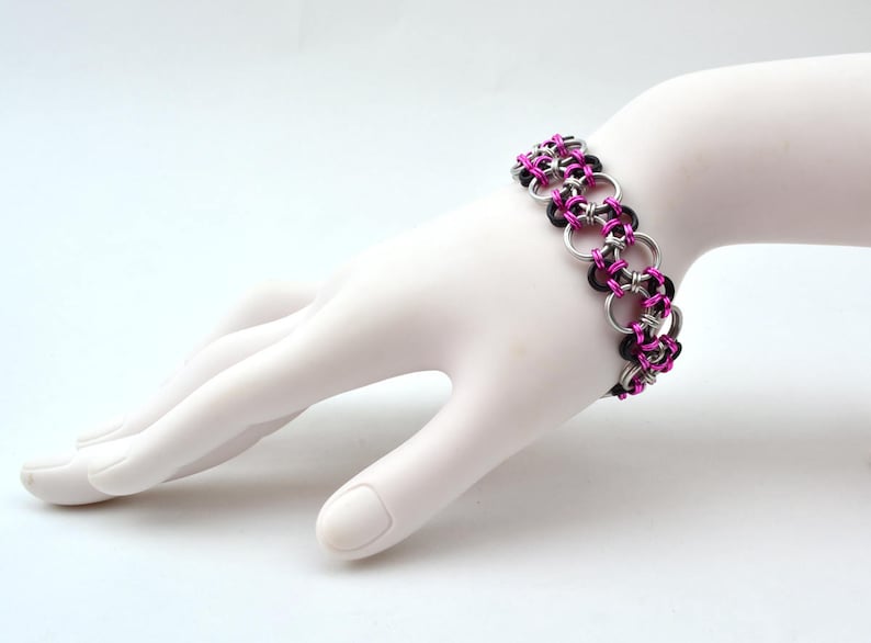 May include: A black and pink chainmail bracelet with silver rings.
