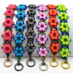 May include: Seven colourful bracelets with flower-shaped links. The bracelets are made of metal and have a variety of colours, including pink, blue, grey, orange, and green. Each bracelet has a small ring at the end.