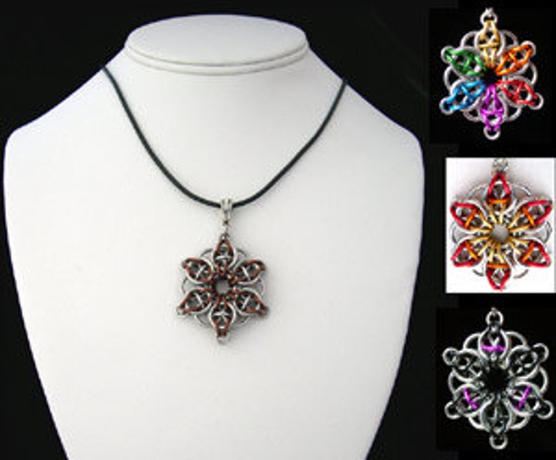 Pode incluir: Um colar com um pingente de floco de neve prateado em um cord&atilde;o de couro preto. O floco de neve &eacute; feito de an&eacute;is de metal entrela&ccedil;ados e tem um esquema de cores vermelho, marrom e dourado.