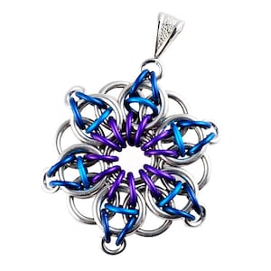 Pode incluir: Um pingente de metal prateado, azul e roxo em forma de flor com uma argola no topo.