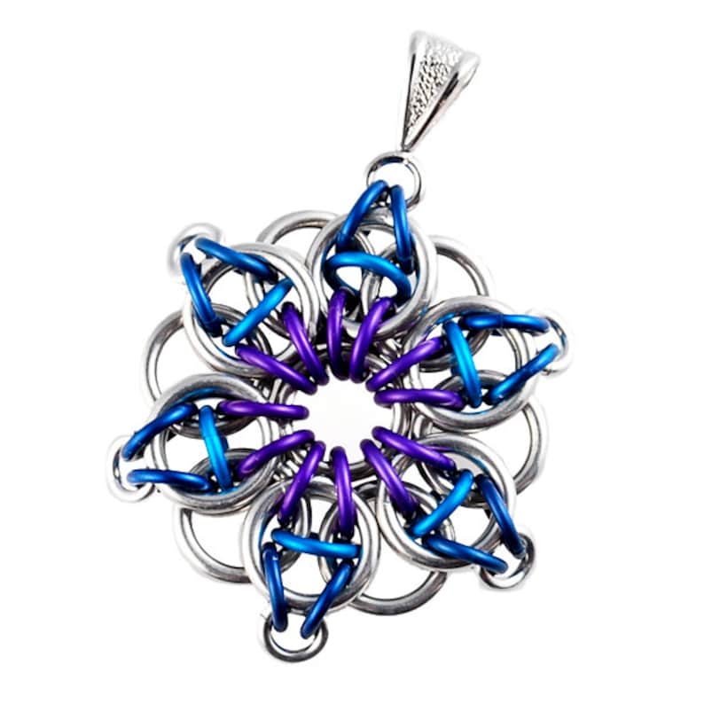 Pode incluir: Um pingente de metal prateado, azul e roxo em forma de flor com uma argola no topo.