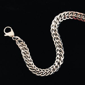 May include: A silver chain bracelet with a lobster clasp closure. The chain is made of interlocking links that form a braided pattern.