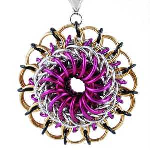 May include: A large, circular pendant made of interwoven metal rings. The rings are in shades of gold, silver, and purple, creating a swirling, flower-like design.