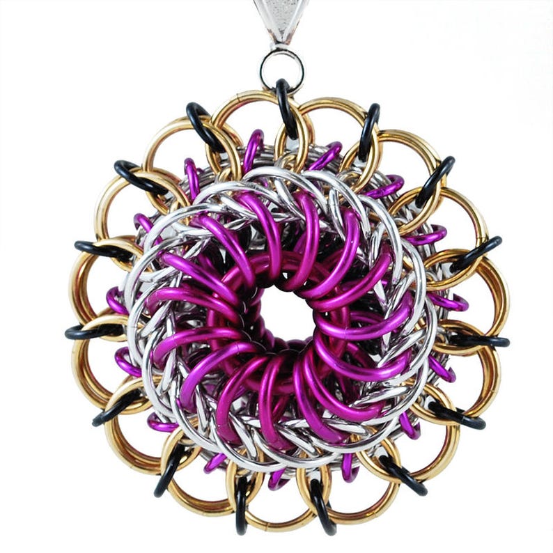 May include: A large, circular pendant made of interwoven metal rings. The rings are in shades of gold, silver, and purple, creating a swirling, flower-like design.