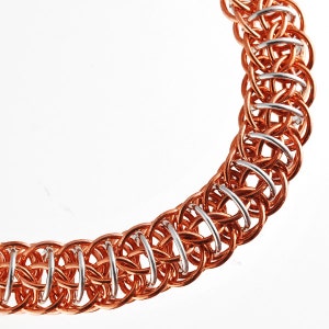 May include: A close-up of a copper and silver chainmail bracelet. The chainmail is made of small, interlocking rings. The bracelet is a beautiful example of craftsmanship.