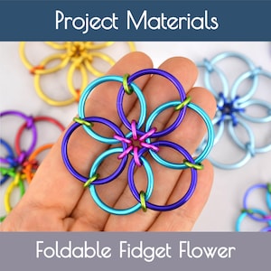 May include: A colorful, foldable fidget flower made of connected metal rings. The flower is held in a hand and features blue, purple, green, and pink rings. The text "Project Materials" and "Foldable Fidget Flower" are displayed.