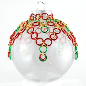 Op de afbeelding: Een transparante glazen kerstbal met een kettingmailontwerp in rood, groen en goud.