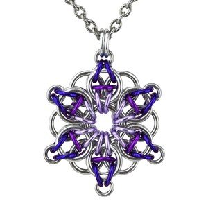 Pode incluir: Colar com corrente prateada e pingente com design de floco de neve. O pingente &eacute; feito de an&eacute;is de metal interligados em prata, roxo e violeta, criando um padr&atilde;o geom&eacute;trico. O colar &eacute; exibido em um fundo branco.