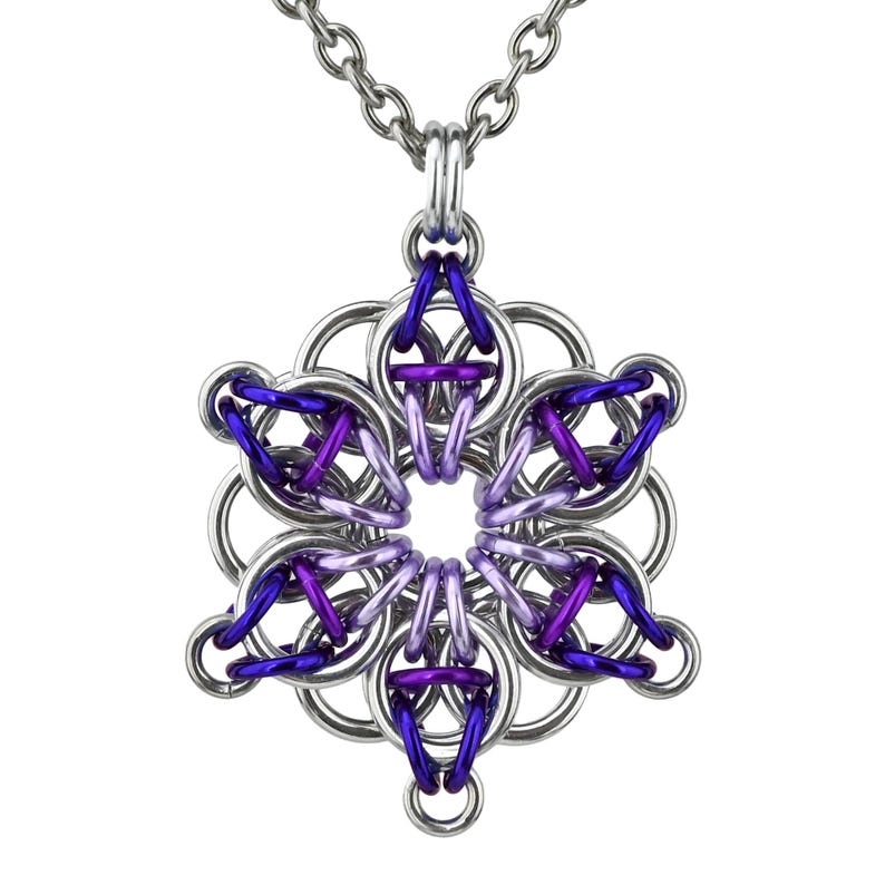 Pode incluir: Colar com corrente prateada e pingente com design de floco de neve. O pingente &eacute; feito de an&eacute;is de metal interligados em prata, roxo e violeta, criando um padr&atilde;o geom&eacute;trico. O colar &eacute; exibido em um fundo branco.