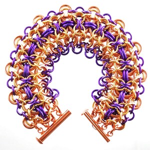May include: A purple and copper chainmail bracelet with a toggle clasp. The bracelet is made of small, interlocking metal rings.