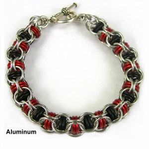 Puede incluir: Un brazalete plateado con anillos negros y rojos. El brazalete est&aacute; hecho de aluminio y tiene un cierre de palanca.