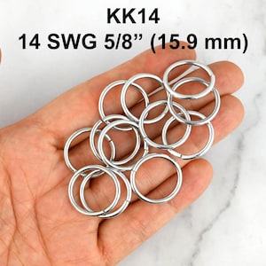 May include: A collection of silver-coloured metal jump rings. The text KK14 and 14 SWG 5/8 inch (15.9 mm) is visible above the rings. These circular metal components feature a smooth, reflective finish and a consistent gauge throughout the set.