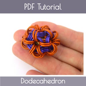 Può includere: Una scultura dodecaedro artigianale realizzata con anelli metallici arancioni e viola. La scultura è tenuta in una mano. L'immagine include il testo "PDF Tutorial" e "Dodecahedron".