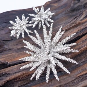 May include: A set of three silver starburst earrings with a textured finish. The earrings are displayed on a piece of wood.