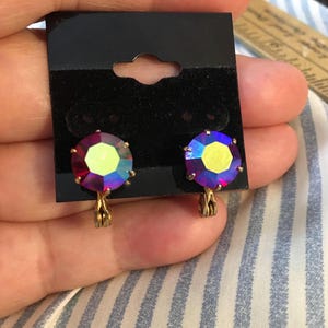 May include: A pair of clip-on earrings with large, iridescent, faceted crystals. The crystals shift in color from red to blue and yellow. The earrings have a gold-colored metal setting and clip.