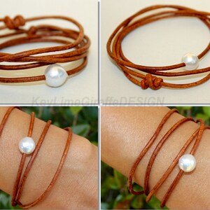 K&ouml;nnte beinhalten: Ein Wickelarmband mit einer gro&szlig;en, wei&szlig;en Perle und mehreren Str&auml;ngen aus braunem Leder. Das Armband ist an den Enden geknotet und wickelt sich mehrmals um das Handgelenk. Das Design ist schlicht und elegant.