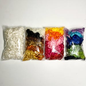 May include: Six bags of colorful curly wool roving. The bags are arranged in a row from left to right: white, brown, orange, pink, blue, and green.