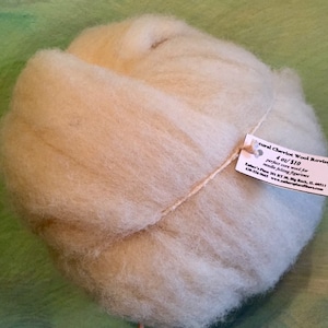 May include: A ball of natural Cheviot wool roving in a light cream color. The wool is tied with twine and has a label attached that reads "Natural Cheviot Wool Roving 4 oz/$10 perfect core wool for needle felting figurines Ether's Place 201 KT 30 Big Rock, IL 60411 630-463-5643 www.ethersplacefibers.com".
