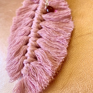 May include: A pink macrame feather keychain with a small, dark red gemstone charm.