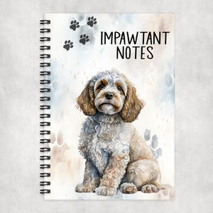 May include: A spiral bound notebook featuring a watercolour illustration of a brown and white cockapoo dog sitting on a light blue and brown background. The notebook cover has the text "Impawtant Notes" printed in black.
