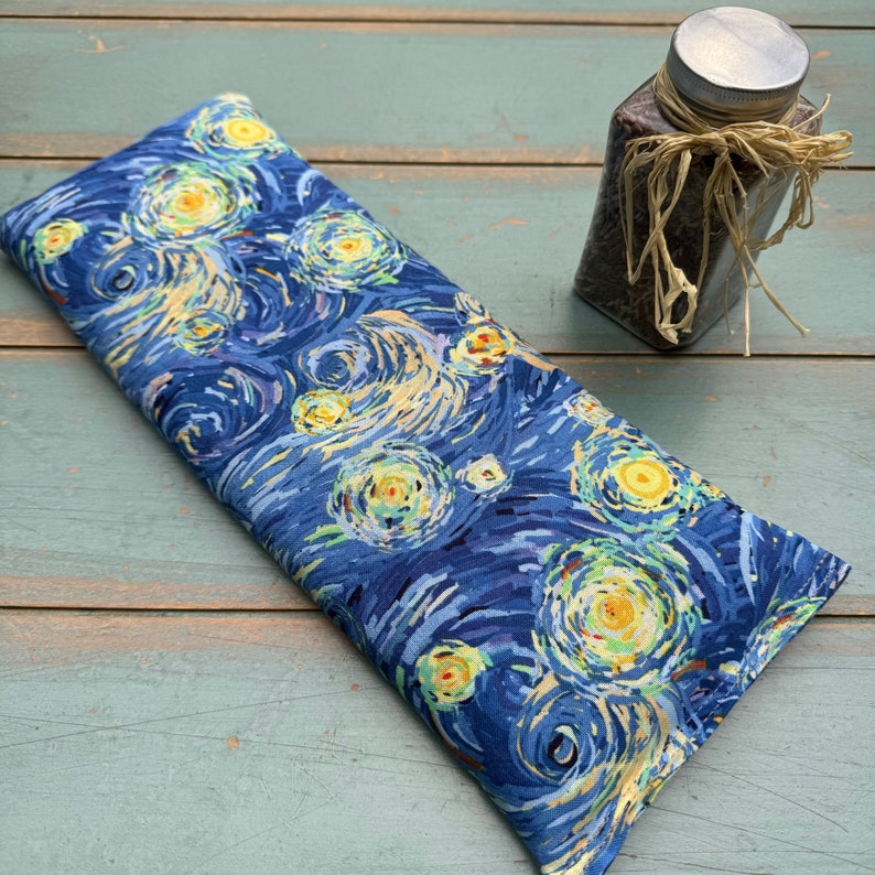 Puede incluir: Una almohada para los ojos de tela azul y amarilla con un patr&oacute;n de remolino que recuerda a la Noche estrellada de Van Gogh. La almohada est&aacute; rellena de semillas de lino y lavanda.