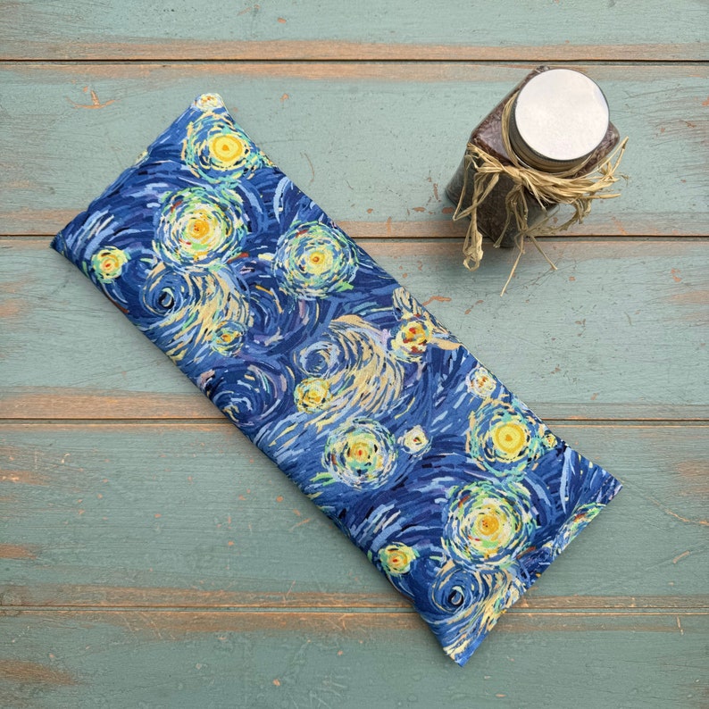 Puede incluir: Una almohada para los ojos de color azul y amarillo con un dise&ntilde;o de remolino que recuerda a la Noche estrellada de Van Gogh. La almohada est&aacute; hecha de tela y est&aacute; rellena de semillas de lino y lavanda.