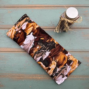 May include: A rectangular fabric item with a horse print in shades of brown, white, and black. A small jar with a silver lid and twine is in the upper right corner. The fabric item is on a light blue wooden surface.
