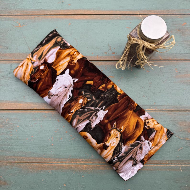 May include: A rectangular fabric item with a horse print in shades of brown, white, and black. A small jar with a silver lid and twine is in the upper right corner. The fabric item is on a light blue wooden surface.