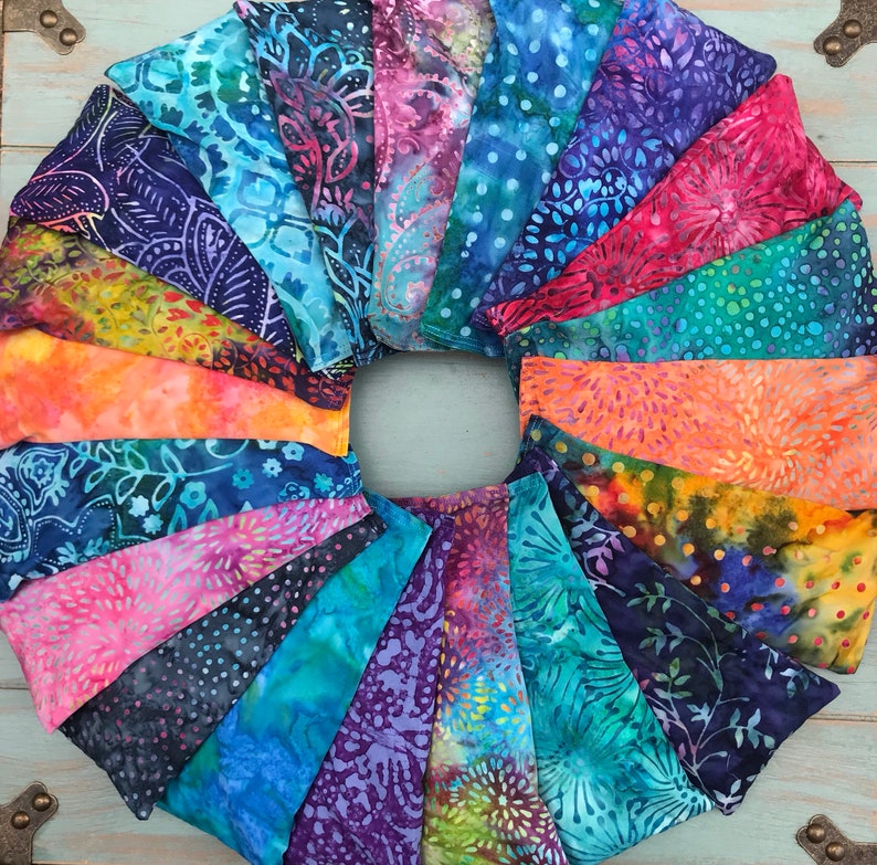 May include: A collection of colorful fabric scraps arranged in a circle, showcasing a variety of patterns and designs. The fabrics are primarily blue, green, and orange with intricate floral and geometric motifs.