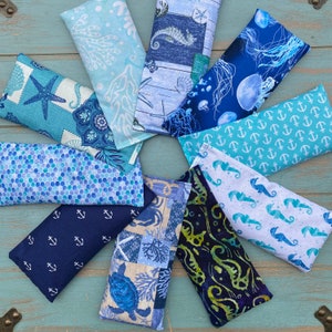 May include: Ten different fabric eye pillows with various nautical themes. The pillows are all rectangular and feature different patterns, including seashells, anchors, seahorses, and jellyfish. The pillows are all made of a soft, comfortable fabric and are perfect for relaxation.