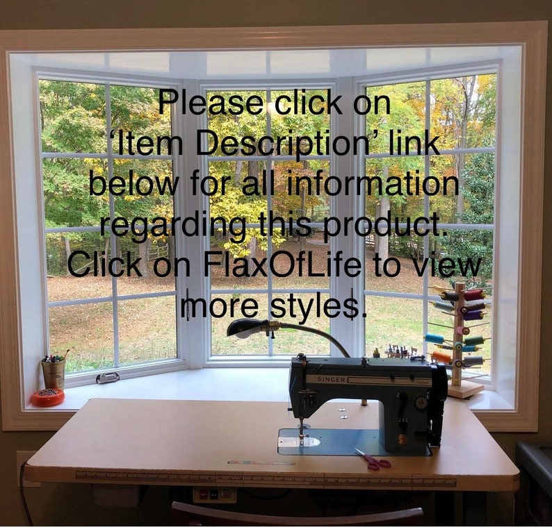May include: A white sewing machine with a black foot pedal and a black lamp on a light brown table. The machine is in front of a window with a view of trees. The text on the machine reads "SINGER". The text on the window reads "Please click on 'Item Description' link below for all information regarding this product. Click on FlaxOfLife to view more styles."