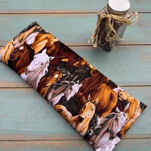 May include: A rectangular fabric item featuring a detailed print of horses in various colors, including brown, white, and black. The horses are depicted in a dynamic composition. A small jar with a silver lid is in the background.