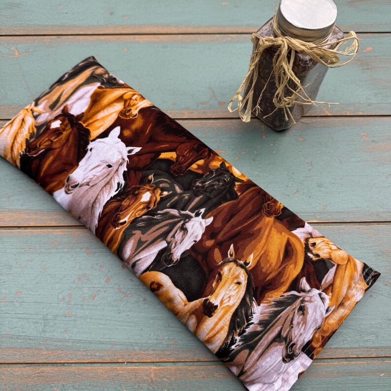 May include: A rectangular fabric item featuring a detailed print of horses in various colors, including brown, white, and black. The horses are depicted in a dynamic composition. A small jar with a silver lid is in the background.