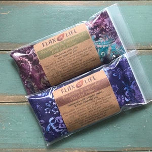 May include: Two purple and blue flax eye pillows in clear plastic bags. The bags have labels that read "Flax of Life" and list the ingredients and instructions for use. The labels are printed on brown paper.